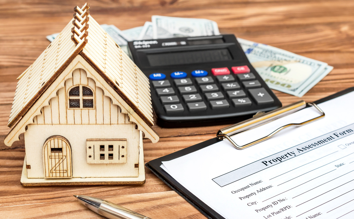 Property assessment form with money, calculator and model of house on the table. Property valuation concept.